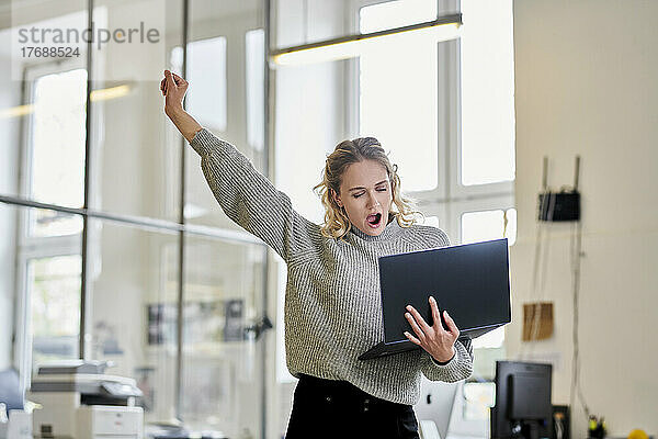 Müde junge Frau im Büro hält Laptop in der Hand und gähnt