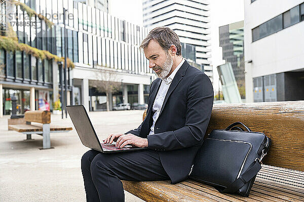 Reifer Geschäftsmann sitzt mit Laptop auf Bank