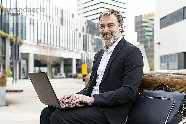Lächelnder Geschäftsmann mit Laptop auf Bank sitzend