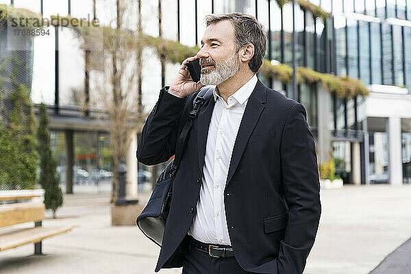 Geschäftsmann spricht mit Smartphone und steht vor Bürogebäude