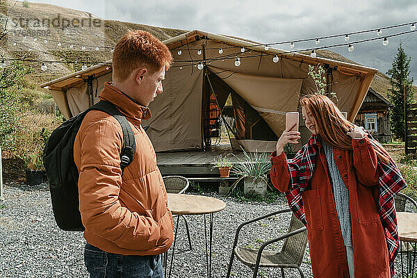 Junge Frau fotografiert ihren Freund per Smartphone im Glamping-Zelt