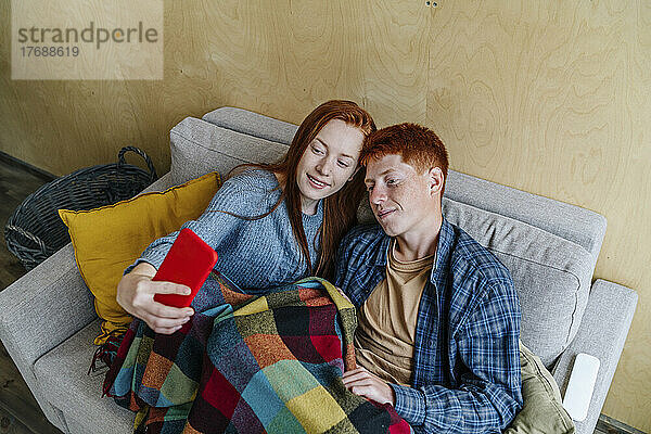 Frau mit Freund macht Selfie per Handy im Wohnzimmer