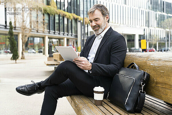 Lächelnder reifer Geschäftsmann mit Tablet-PC auf Bank sitzend