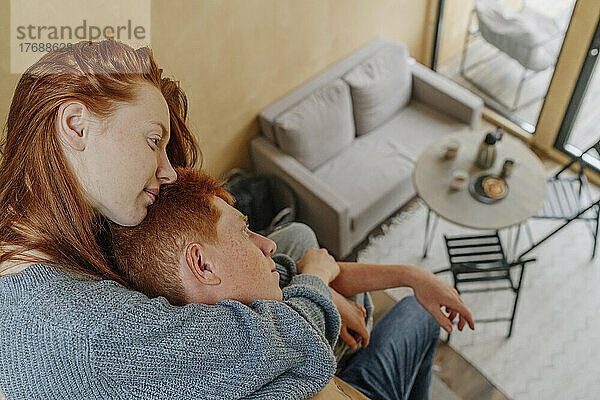Junge Frau umarmt ihren Freund von hinten im Wohnzimmer
