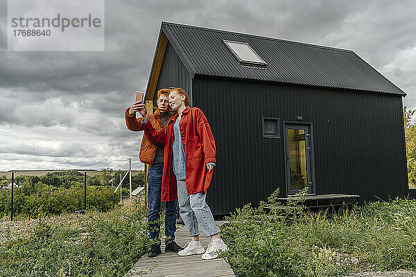 Junges Paar macht ein Selfie vor einem Tiny House