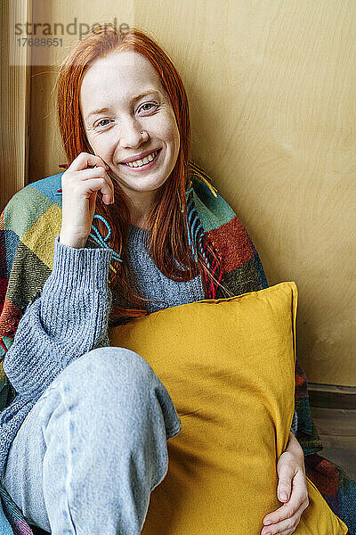 Smiling young woman with pillow in front of wall