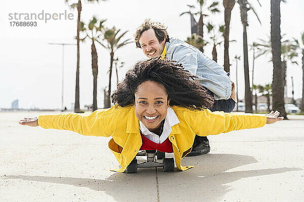 Happy man with playful woman lying on skateboard at footpath