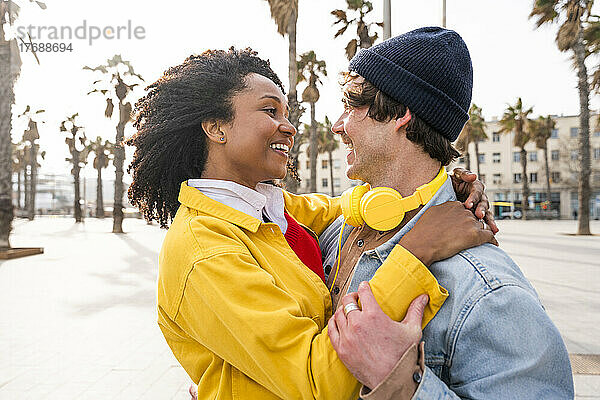Lächelnde Frau mit Afro-Frisur blickt Mann mit Strickmütze an