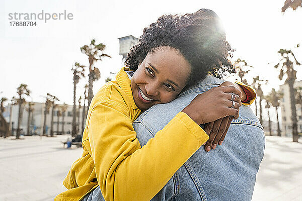 Glückliche Frau mit Afro-Frisur umarmt Mann an sonnigem Tag