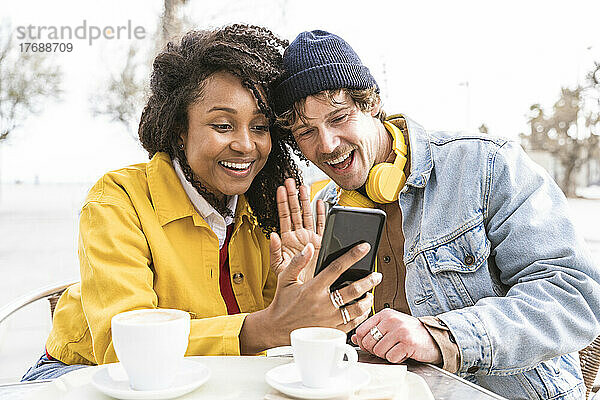 Glückliche Frau und Mann winken per Videoanruf per Smartphone im Straßencafé