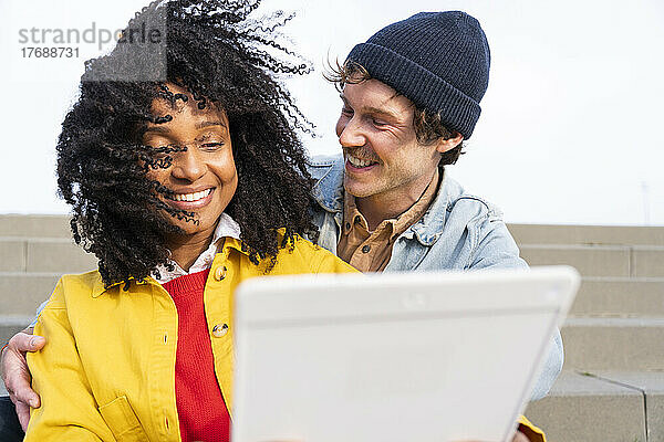 Glücklicher Mann schaut Freundin mit zerzausten Haaren per Tablet-PC an