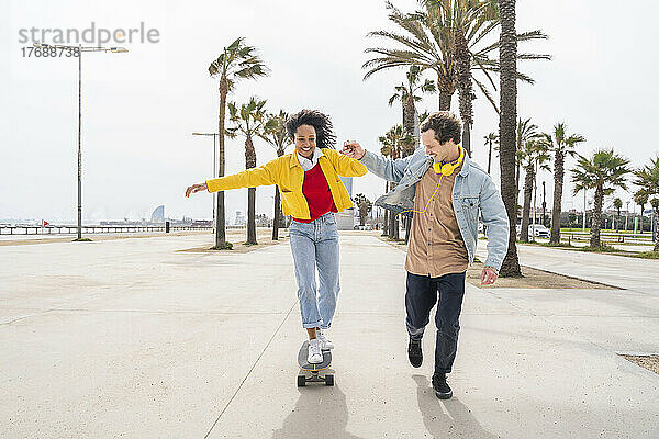 Glücklicher Mann bringt Frau auf Fußweg Skateboardfahren bei
