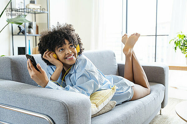 Schöne Frau mit Kopfhörern und Smartphone  die zu Hause auf dem Sofa liegt