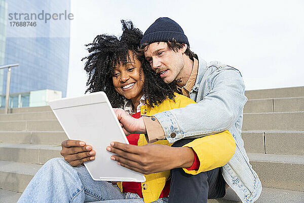 Glückliche Frau teilt Tablet-PC mit Freund  der auf Stufen sitzt