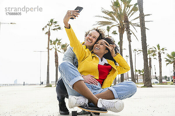 Glückliche Frau mit Mann macht Selfie per Smartphone auf Skateboard