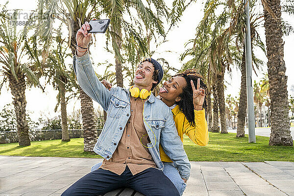 Glückliches Paar streckt die Zunge heraus und macht im Park ein Selfie mit dem Handy