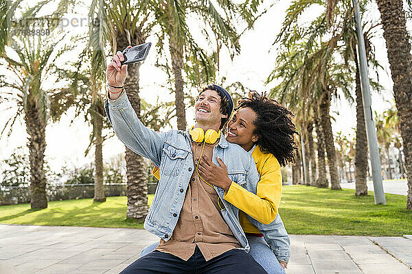 Glücklicher Mann macht Selfie mit Freundin per Smartphone im öffentlichen Park