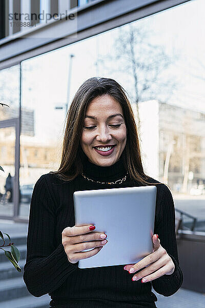 Lächelnde junge Geschäftsfrau mit Tablet-PC  die vor dem Gebäude steht