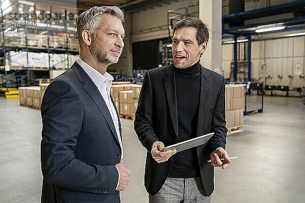 Reifer Geschäftsmann hält Tablet-PC in der Hand und diskutiert mit Kollegen in der Fabrik