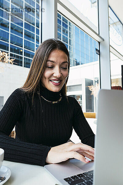 Lächelnde junge Geschäftsfrau benutzt Laptop im Café