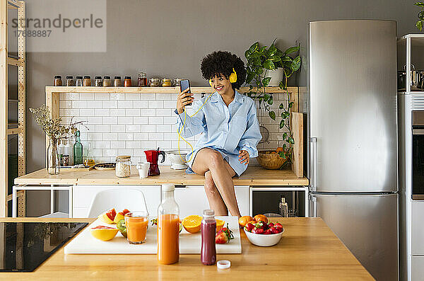 Glückliche Frau  die zu Hause auf der Küchentheke sitzt und ein Selfie mit ihrem Smartphone macht
