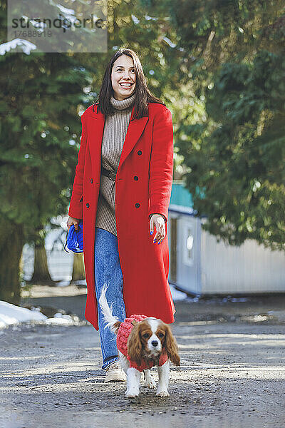 Cheerful young woman with pet dog walking on footpath