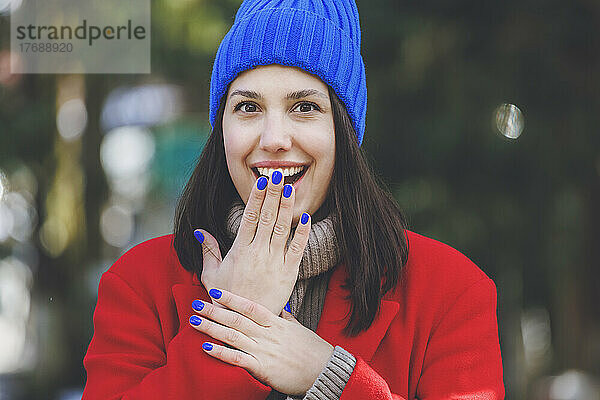 Überraschen Sie junge Frau mit blauem Nagellack  der den Mund mit der Hand bedeckt