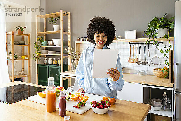 Glückliche Frau mit Tablet-PC  die zu Hause in der Küche steht