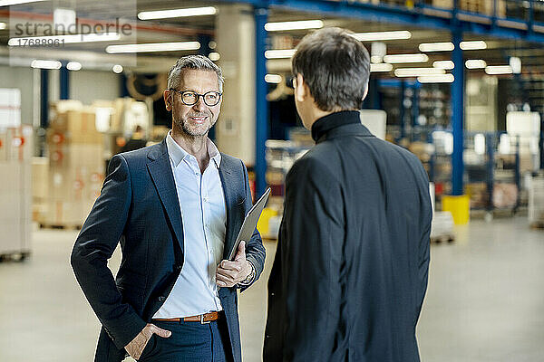 Reifer Geschäftsmann mit der Hand in der Tasche diskutiert mit Kollegen in der Fabrik