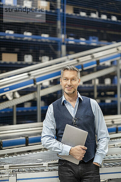 Reifer Geschäftsmann mit der Hand in der Tasche in der Fabrik