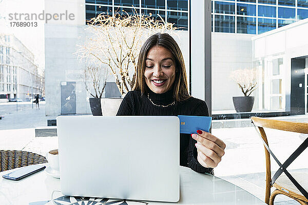 Glückliche Geschäftsfrau mit Kreditkarte und Laptop im Café sitzend