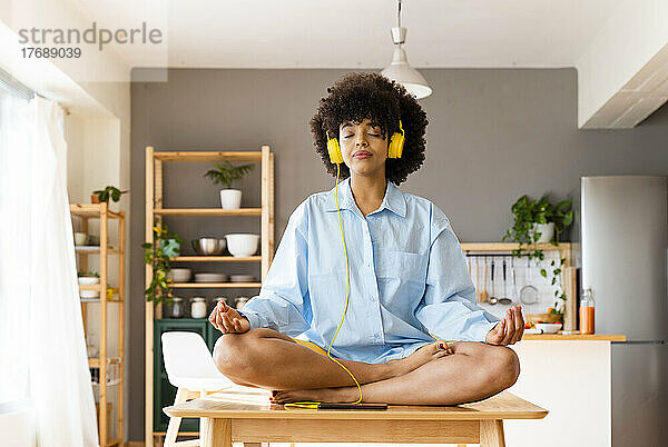 Schöne Frau mit Kopfhörern meditiert zu Hause am Esstisch