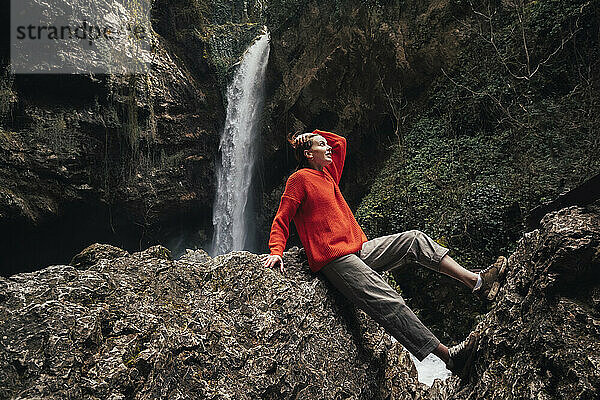 Junge Frau sitzt auf einem Felsen vor dem Wasserfall