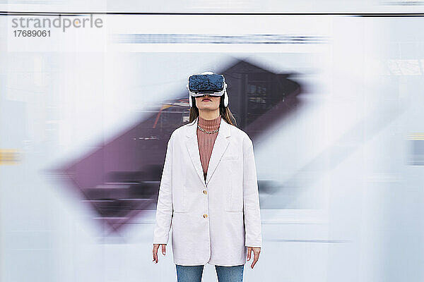 Businesswoman wearing virtual reality simulator standing in front of wall