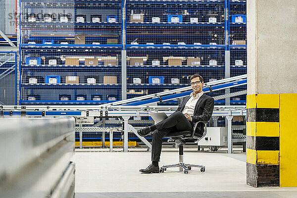 Confident mature businessman sitting on chair at warehouse