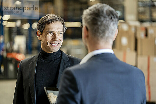 Lächelnder Geschäftsmann diskutiert mit Kollegen in der Fabrik