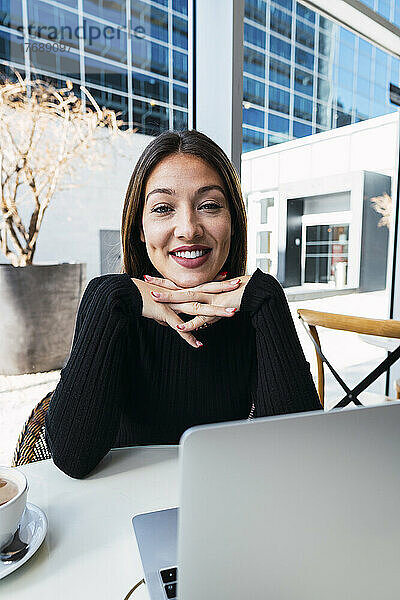 Lächelnde Geschäftsfrau mit gefalteten Händen sitzt im Café
