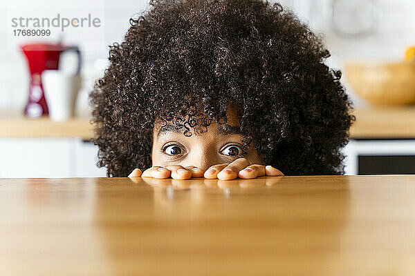 Frau mit Afro-Frisur versteckt sich zu Hause hinter der Kücheninsel