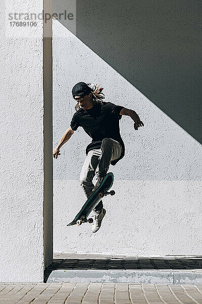 Mann mit Skateboard springt vor Wand