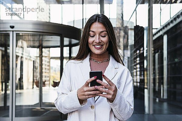 Glückliche Geschäftsfrau  die im Bürogebäude ihr Mobiltelefon benutzt