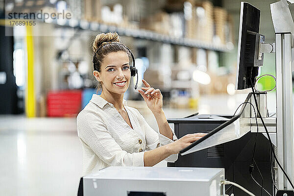 Lächelnde Geschäftsfrau mit Headset am Computer in der Fabrik