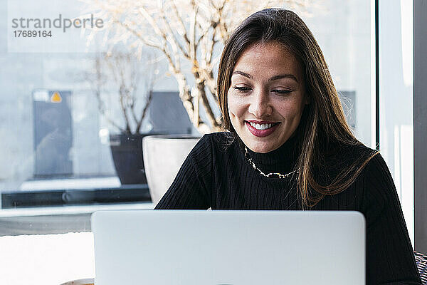 Lächelnde junge Geschäftsfrau mit braunen Haaren  die im Café einen Laptop benutzt