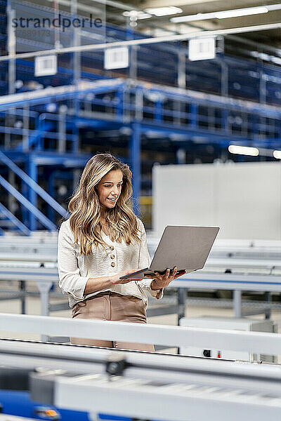 Junge Geschäftsfrau benutzt Laptop bei der Arbeit in der Fabrik