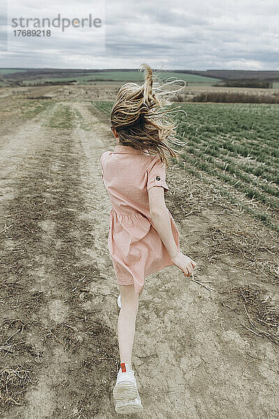 Girl running on dirt road in agricultural field