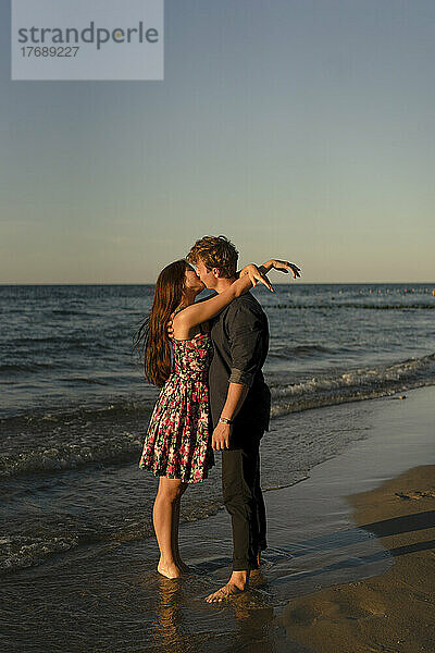 Junges  liebevolles Paar küsst sich am Strand bei Sonnenuntergang