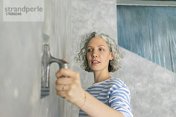 Frau arbeitet mit Arbeitsgerät an grauer Wand