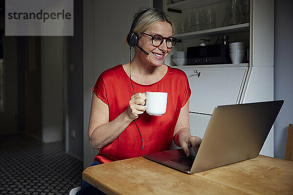 Lächelnde Frau mit Headset  Laptop und Teetasse am Tisch