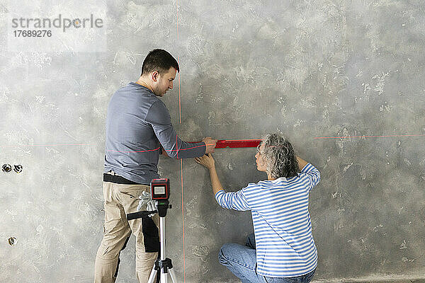 Frau und Freundin messen Baulaserniveau an grauer Wand