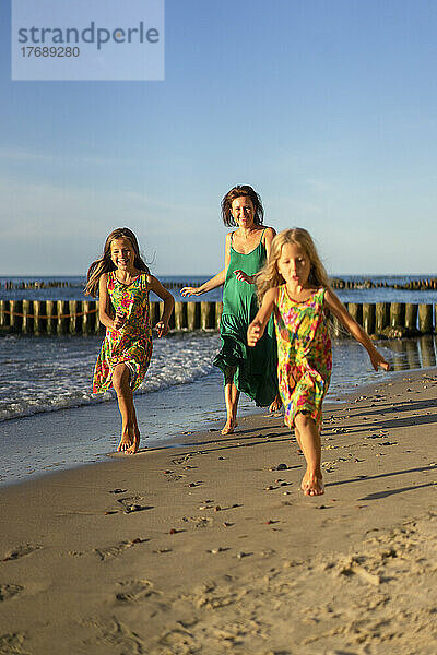 Glückliche Mutter mit Töchtern  die am Strand laufen