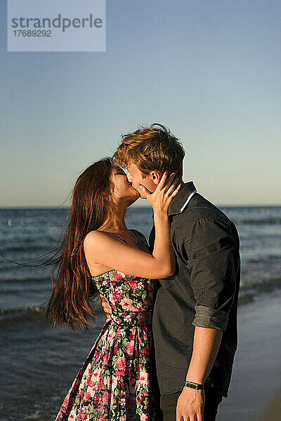 Liebevolles Paar küsst sich am Strand bei Sonnenuntergang